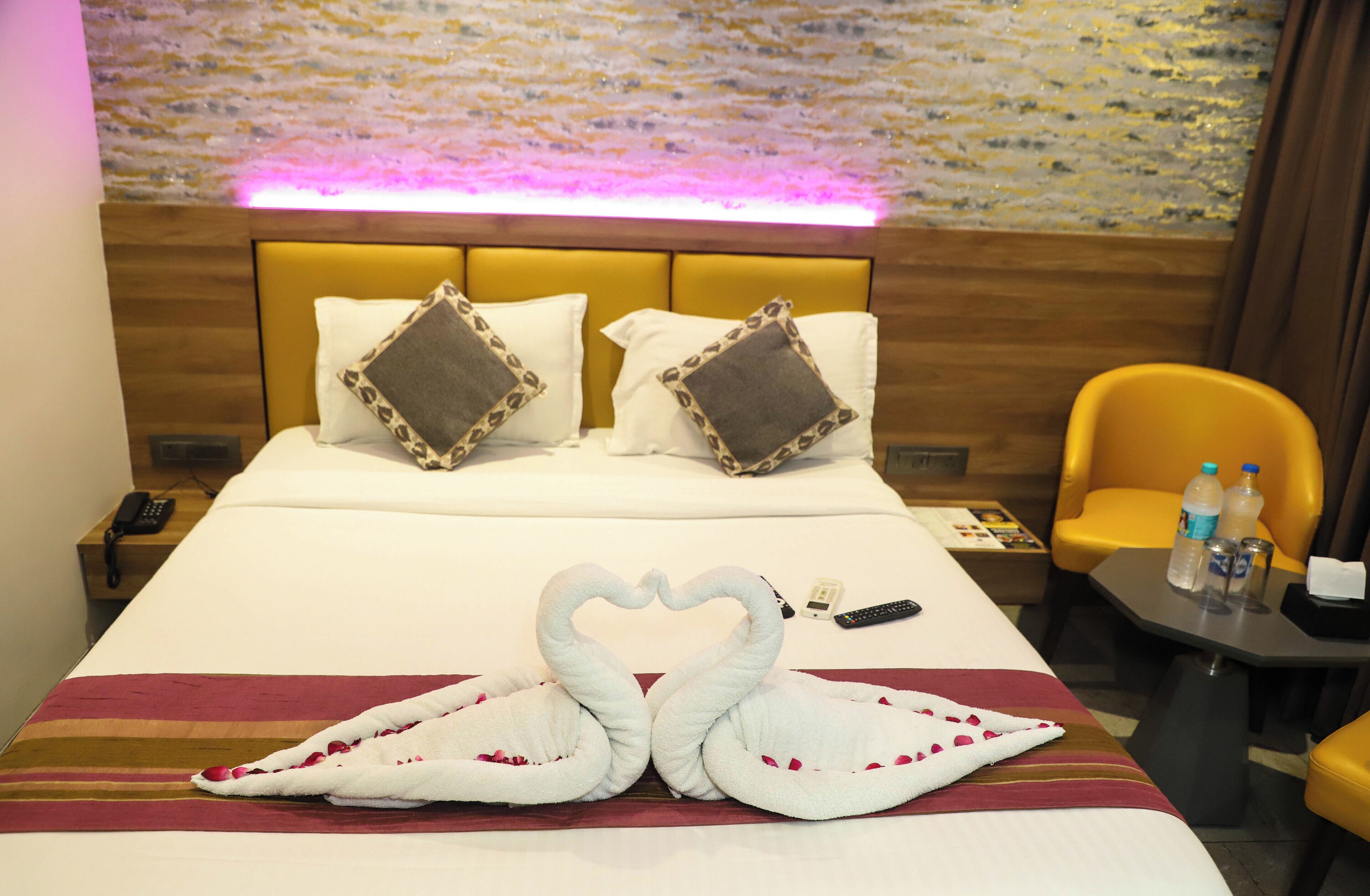A hotel room with a bed, two pillows, a bedside table with a remote control, a chair, and a wall with a textured pattern.