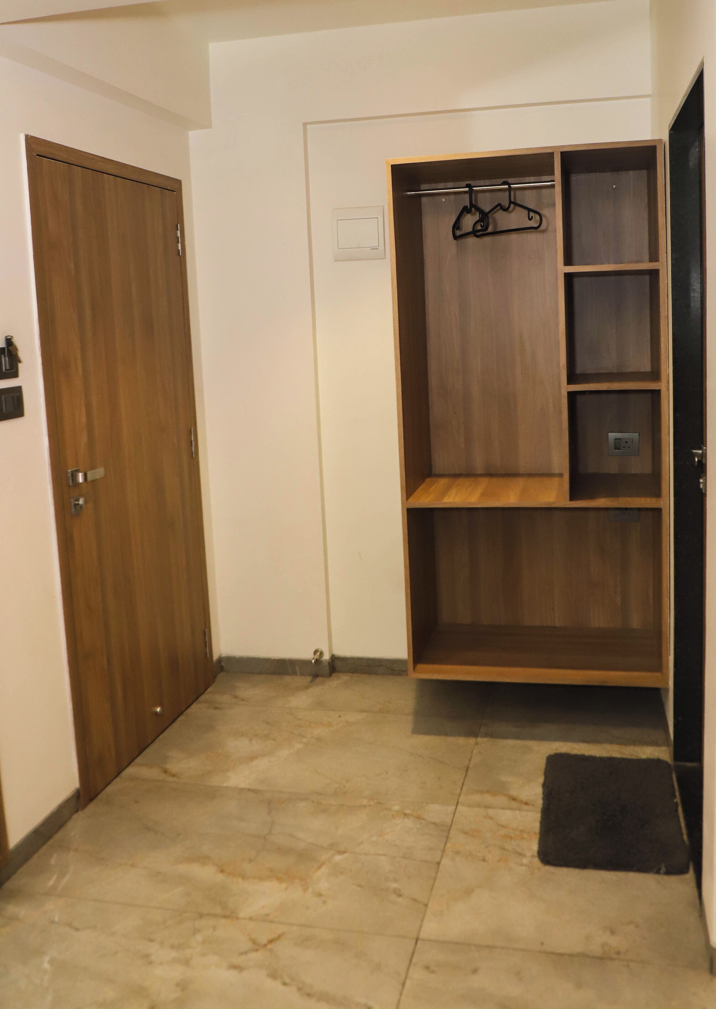 A hallway with a wooden door, a closet with shelves and a hanging rack, and a tiled floor.