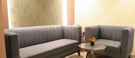 A modern living room with two grey sofas, a small round table with a potted plant, and a textured wall.
