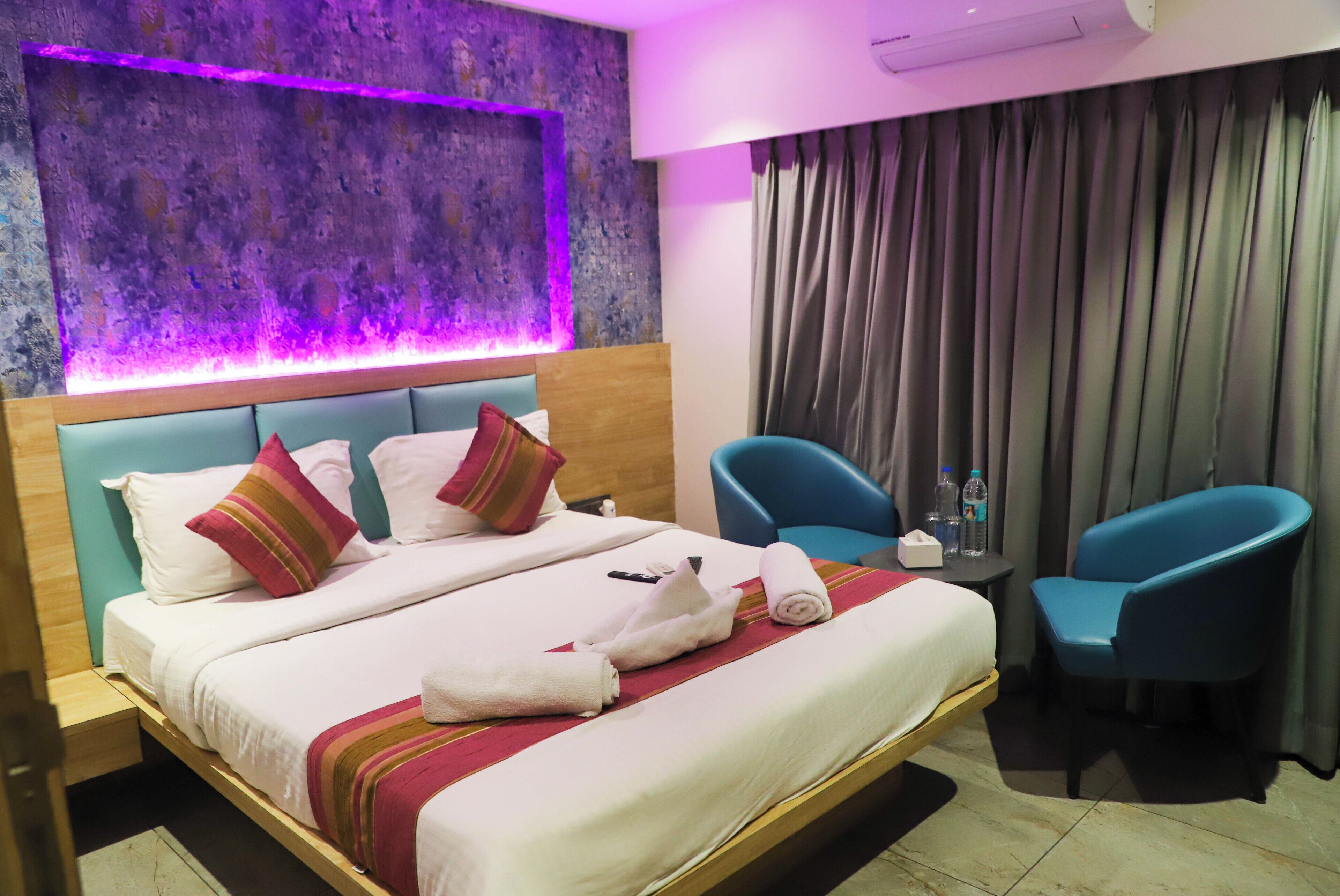A hotel room with a bed, two chairs, a table with bottles, and a wall with a textured design.