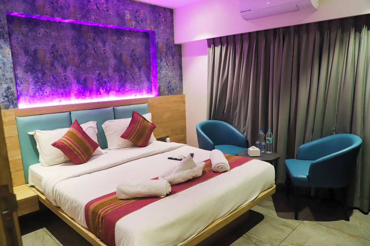 Quarto de hotel com cama, duas cadeiras, uma mesa com garrafas e parede com textura.