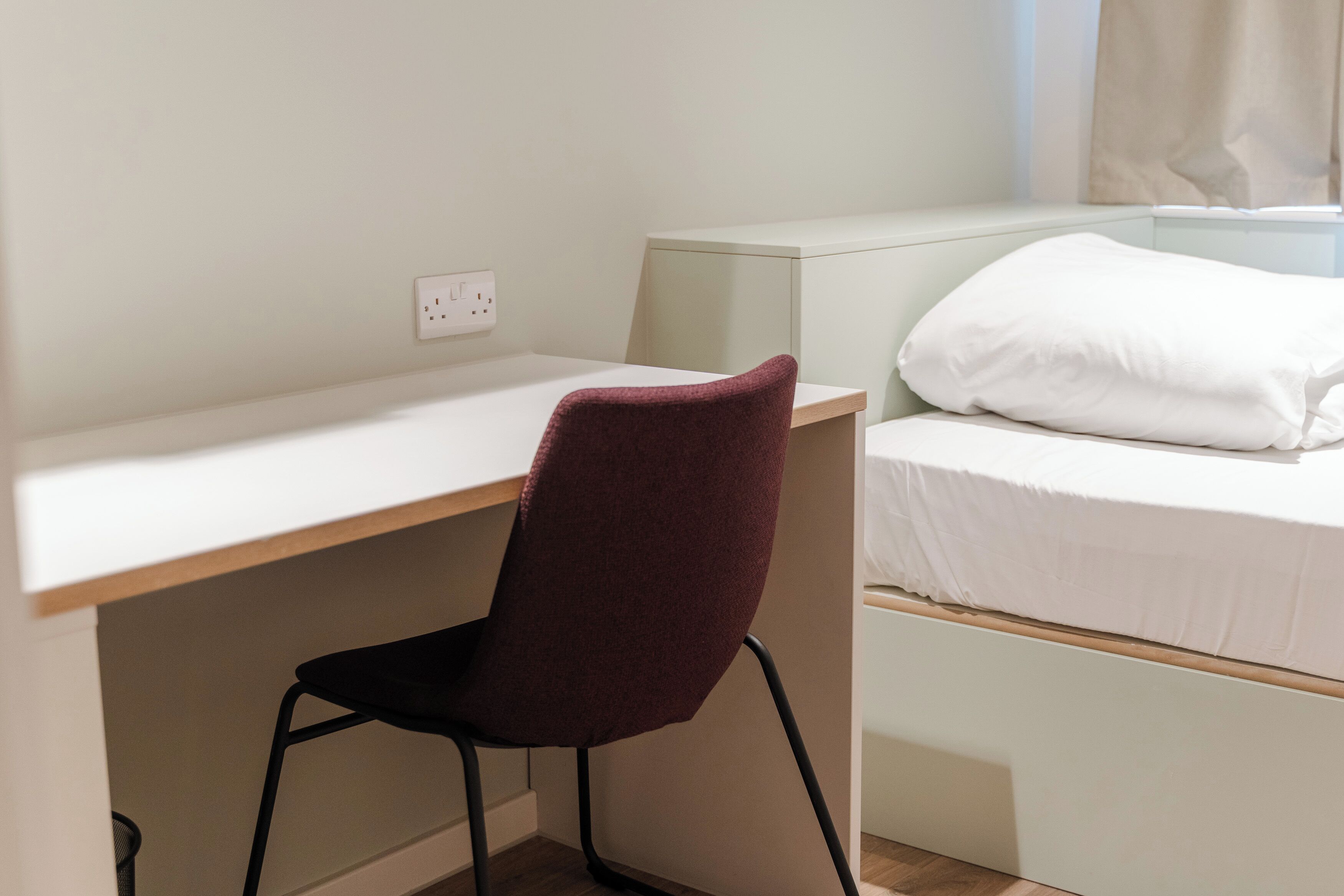 A small, neatly organized room with a desk, a chair, and a bed.