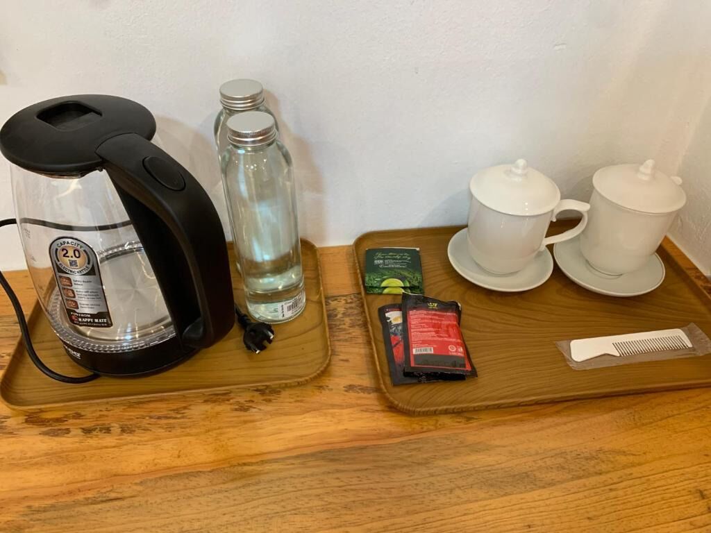 A coffee maker, a water bottle, a packet of sugar, a packet of creamer, and a spoon on a wooden tray.