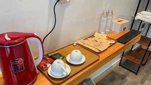 A hotel room with a wooden counter, a red electric kettle, two white cups, a tray with tea bags, and a trash bin. - Thành Nam Hotel (Dien Bien Phu)