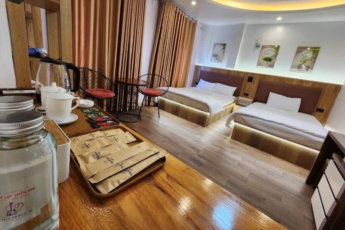 A hotel room with a wooden floor, two beds, a small table with a kettle and cups, and a chair.