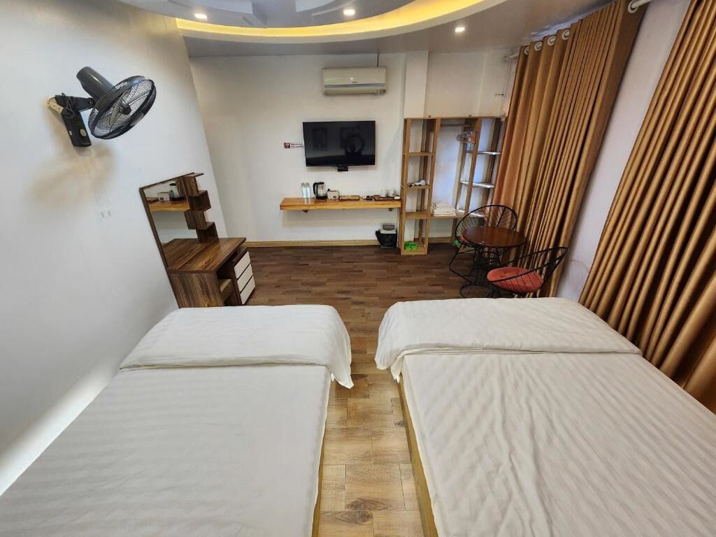 Ett hotellrum med två sängar, en TV, en fläkt, en hylla med toalettartiklar och en stol.