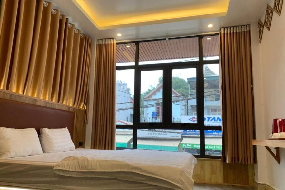 A hotel room with a large bed, wooden headboard, and a view of the outside through large windows.