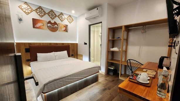 A modern hotel room with a wooden bed, a dining table with a tray, and a shelf unit. - Thành Nam Hotel (Dien Bien Phu)