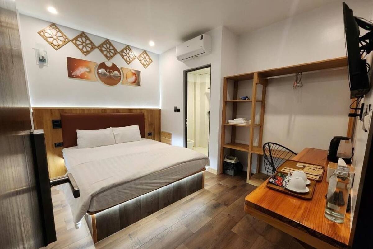 A modern hotel room with a wooden bed, a dining table with a tray, and a shelf unit.