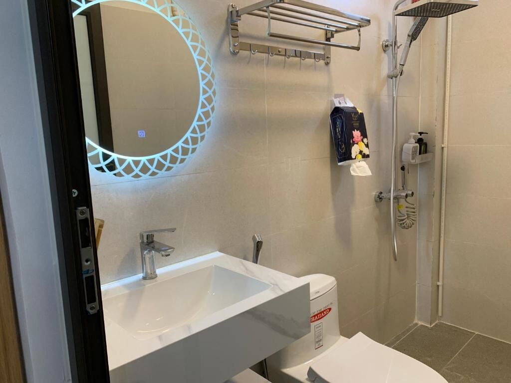 A modern bathroom with a white sink, a mirror with a geometric light fixture, a shower area, and a towel rack.