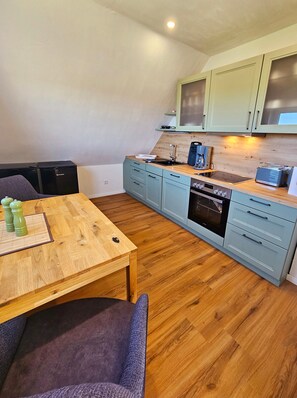 A compact kitchen with a wooden table, a built-in oven, and light blue cabinets. - Apartment 'Matje' with Lake View, Shared Terrace and Wi-Fi (Langeneß)