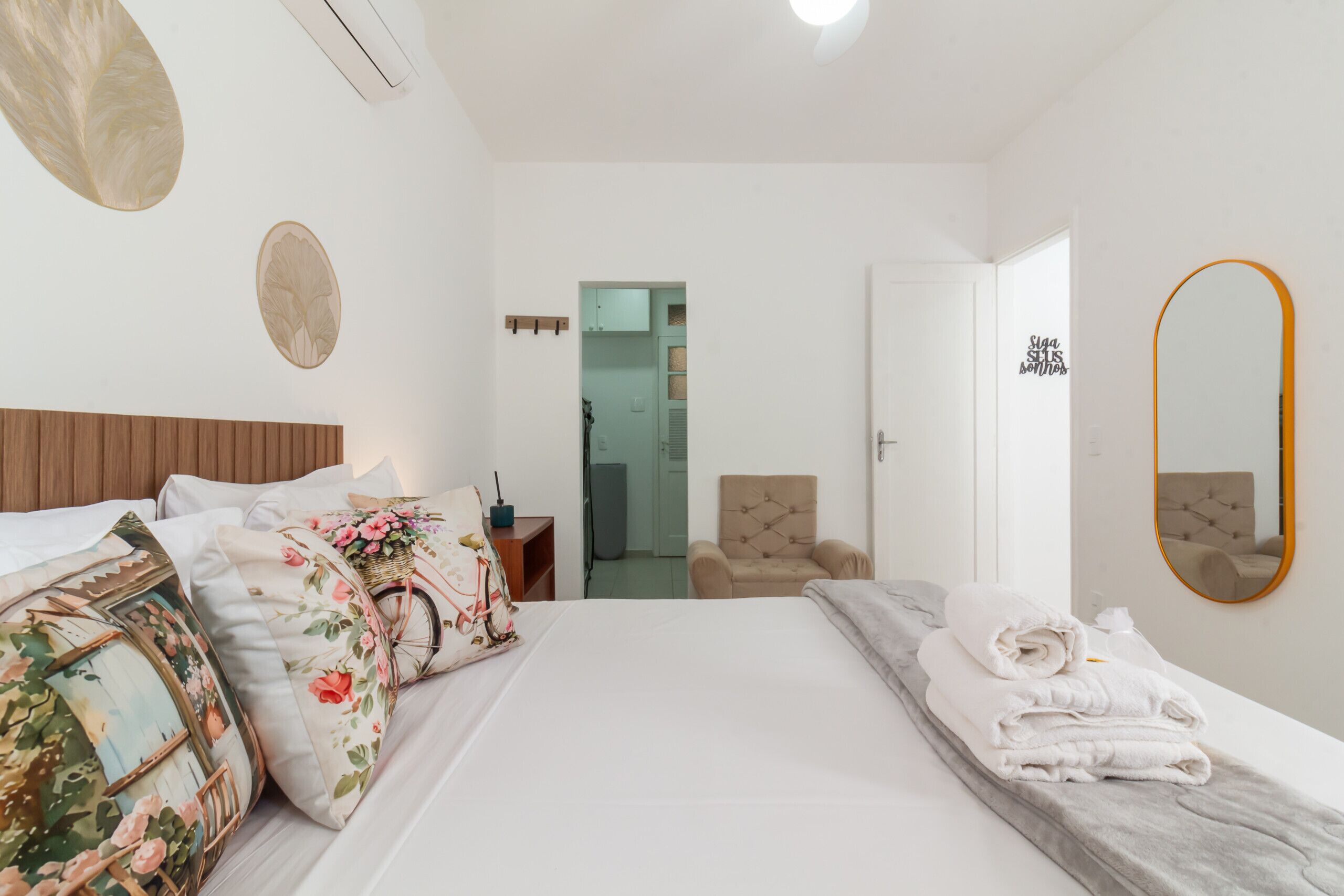 Una camera d'albergo con un letto grande, una sedia, uno specchio e una porta che dà su un'altra stanza.