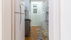 Un pasillo estrecho con suelo de baldosas, una puerta blanca y un refrigerador a la izquierda.