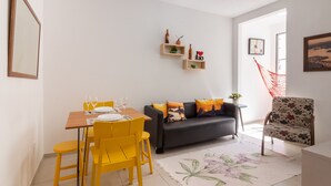 Un comedor con una mesa de madera y sillas amarillas, un sofá gris con cojines coloridos y una alfombra con estampado floral.