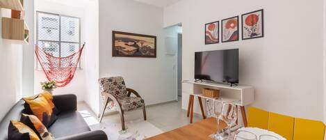 A modern living room with a sofa, a dining table set for two, a TV, and a hammock.
