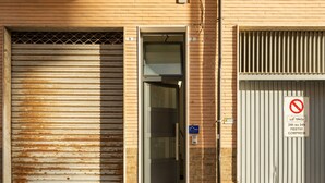 A building with a closed metal shutter door, a glass door entrance, and a no parking sign.