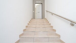 A staircase leading to a door with a 'Welcome' sign, a handrail, and a plain wall.