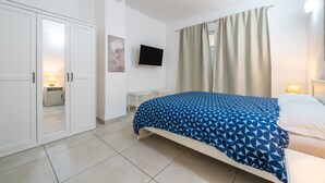A bedroom with a bed, a TV, a wardrobe, and a window with curtains.