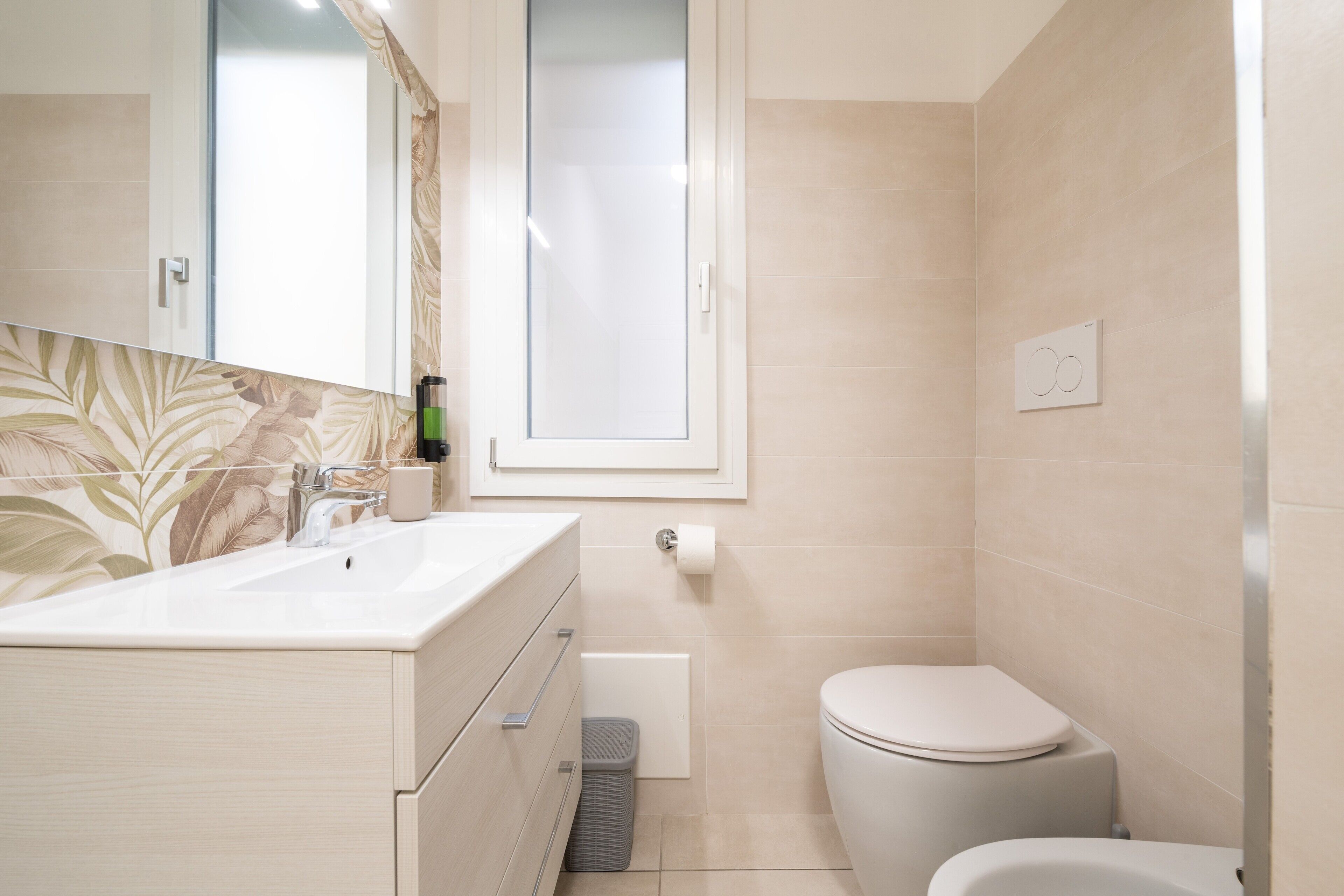 Une salle de bain équipée d’un lavabo, d’un miroir, de toilettes et d’une poubelle.