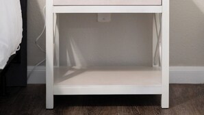 Et hvidt natbord med en skuffe, en hvid lampe og en potteplante.