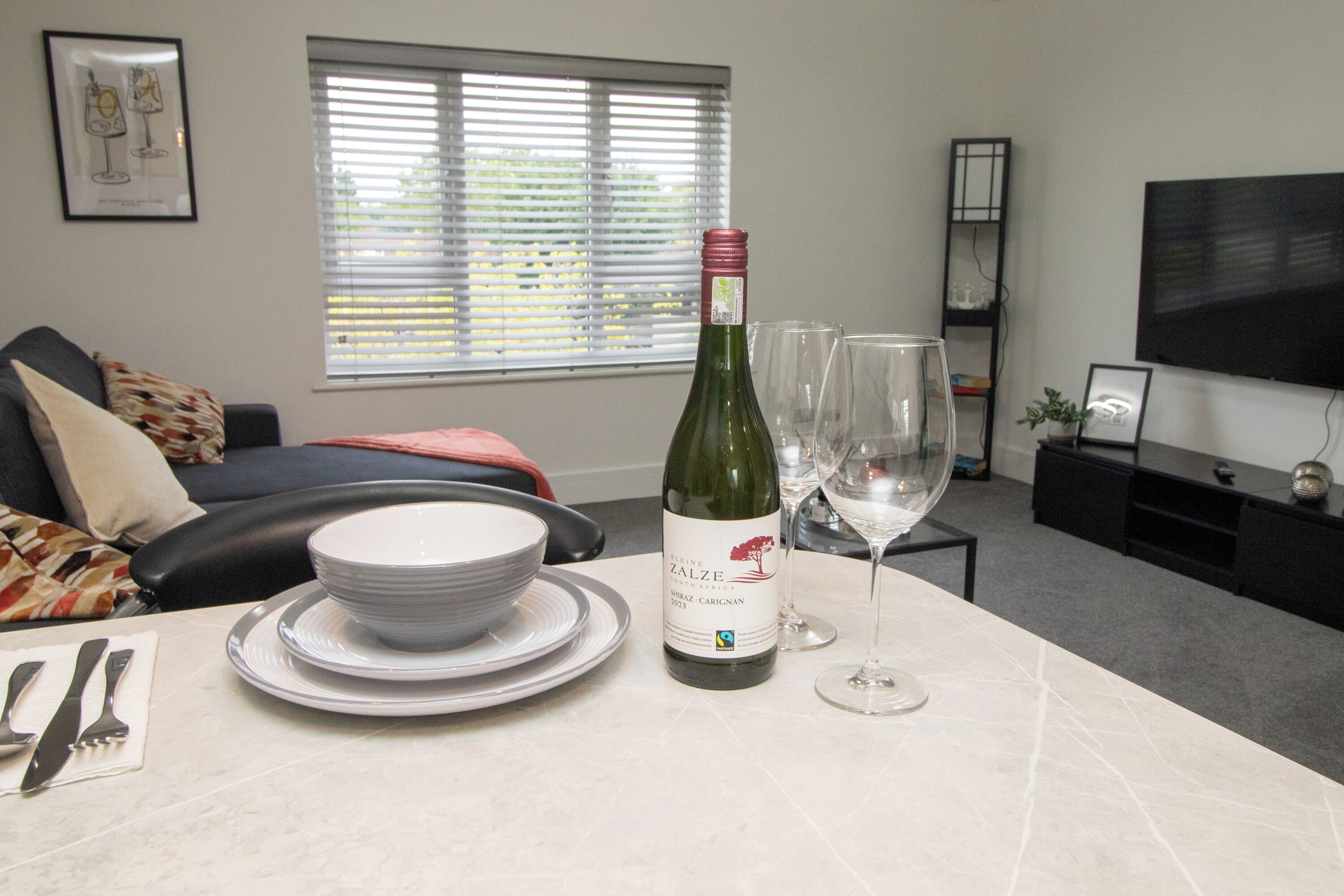 A living room with a dining table set for two, a bottle of wine, and two wine glasses.