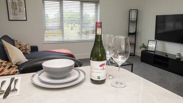 A living room with a dining table set for two, a bottle of wine, and two wine glasses.