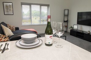 A living room with a dining table set for two, a bottle of wine, and two wine glasses. - VELVET VISTA (Basildon)