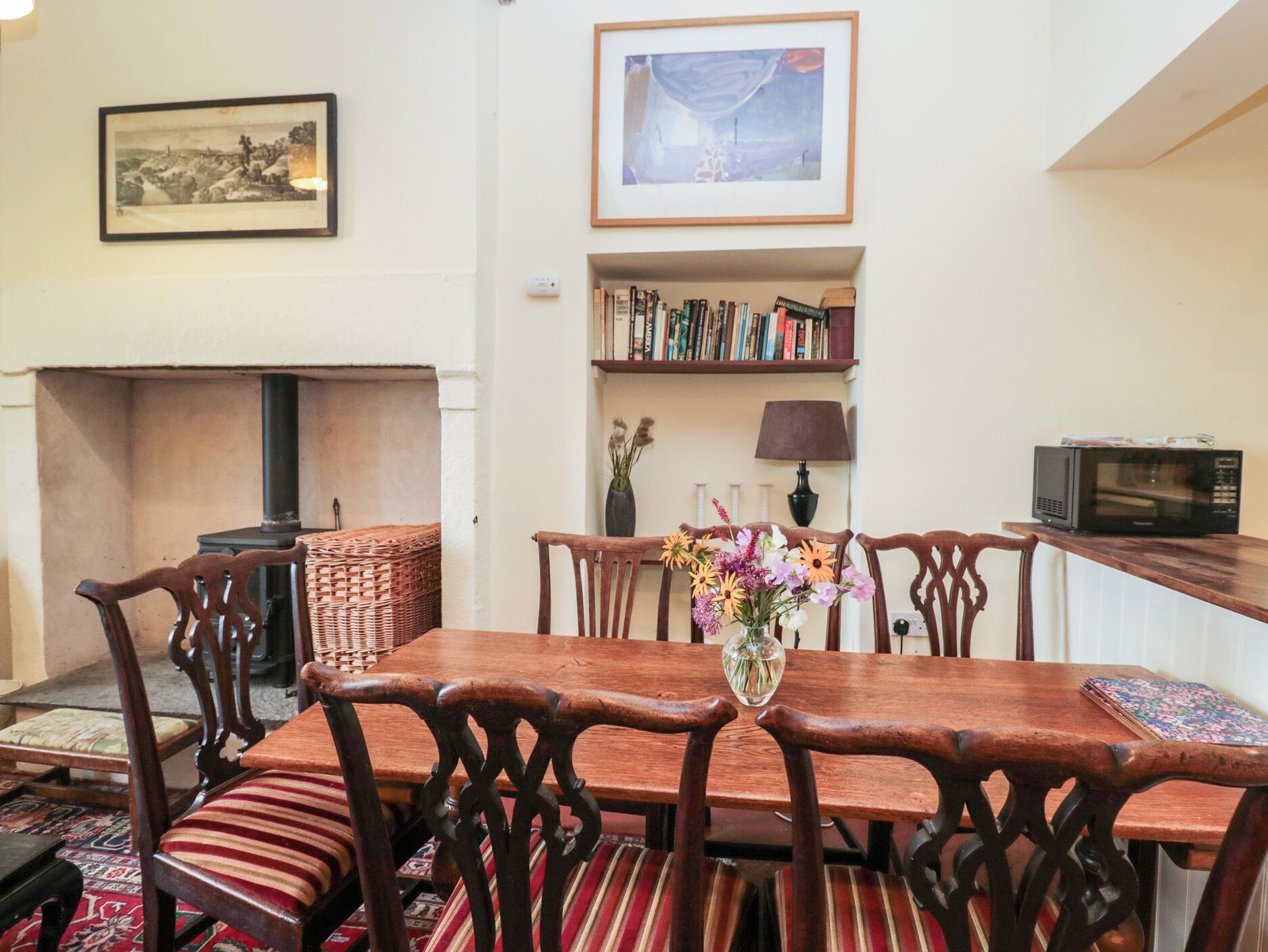 A dining area with a wooden table and chairs, a fireplace, a bookshelf, and a framed picture on the wall.