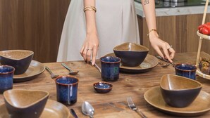 A person arranging bowls on a table in a kitchen with wooden cabinets and a green wall. - Fusia Hotel & Apartment (Da Nang)