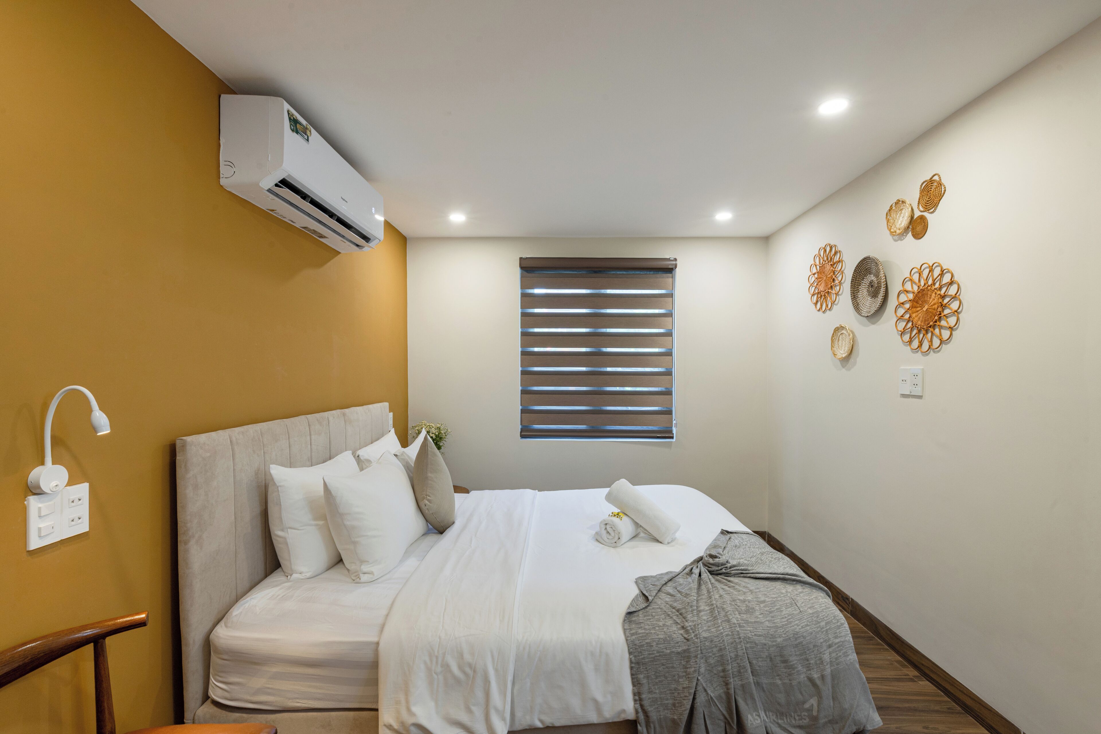 A hotel room with a bed, an air conditioning unit, a window with blinds, and wall decor.
