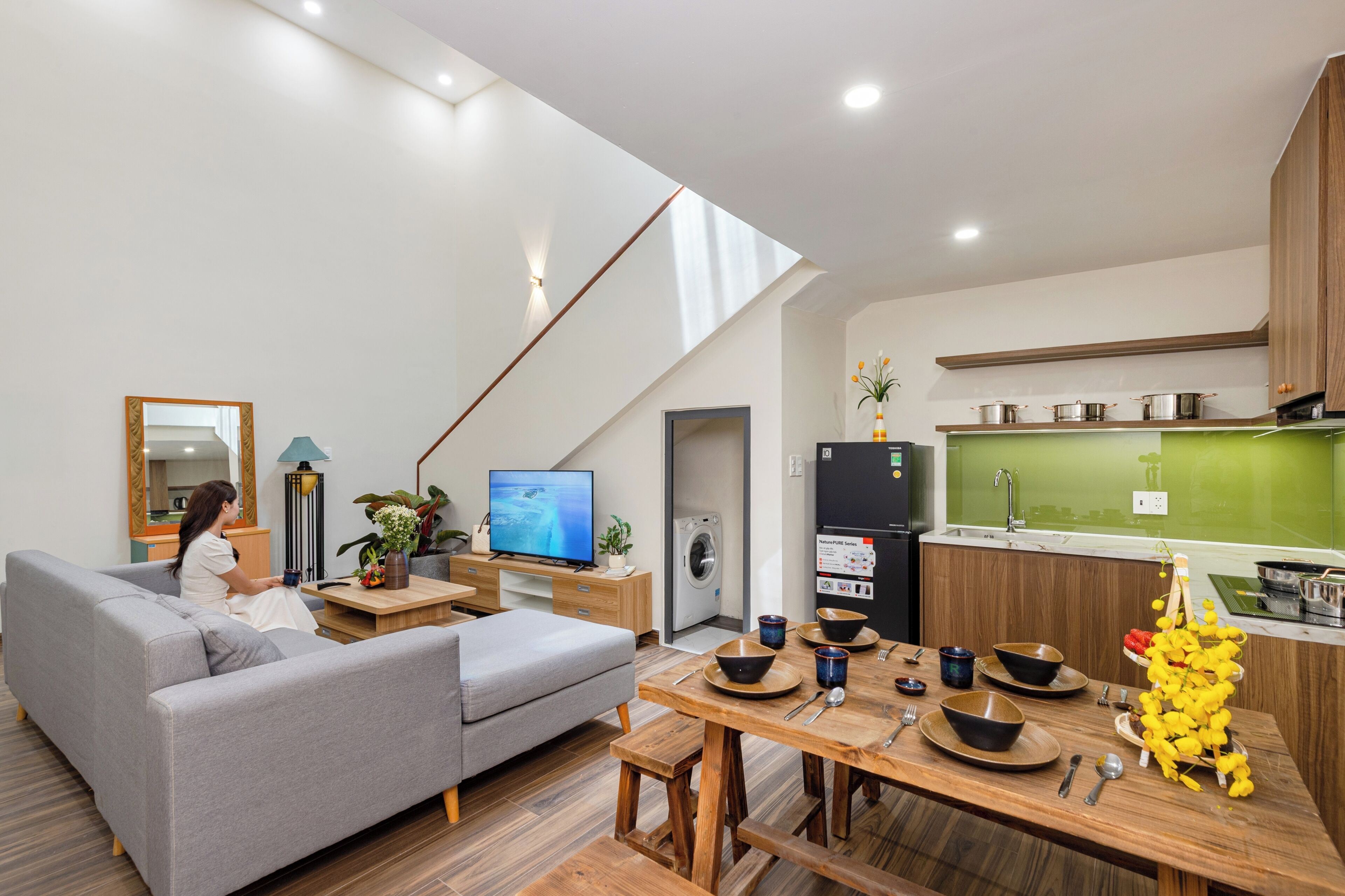 A modern living room with a sofa, TV, and dining area with a table set for two.