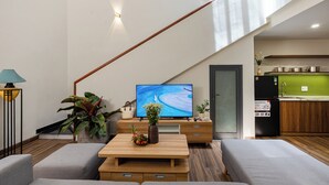 A modern living room with a sofa, coffee table, TV, and a staircase leading to a kitchen. - Fusia Hotel & Apartment (Da Nang)