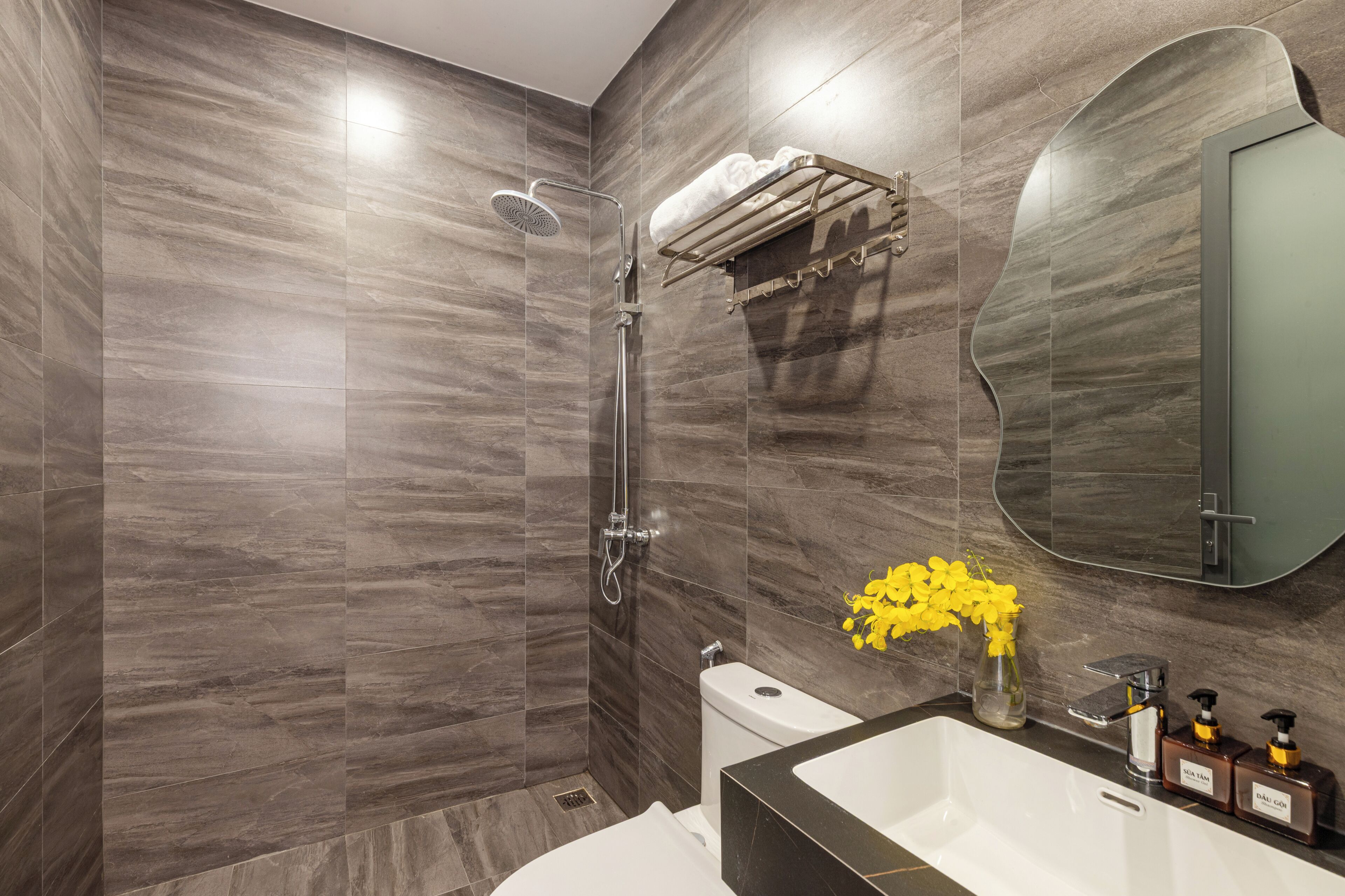 A modern bathroom with a shower, toilet, and sink, featuring a marble wall and a mirror.