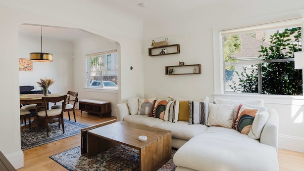 A living room with a sofa, coffee table, and dining area with chairs and a table. There are shelves on the wall and a window with a view of the outside. - Allura Oakland Your Private Sanctuary in the City (Oakland)