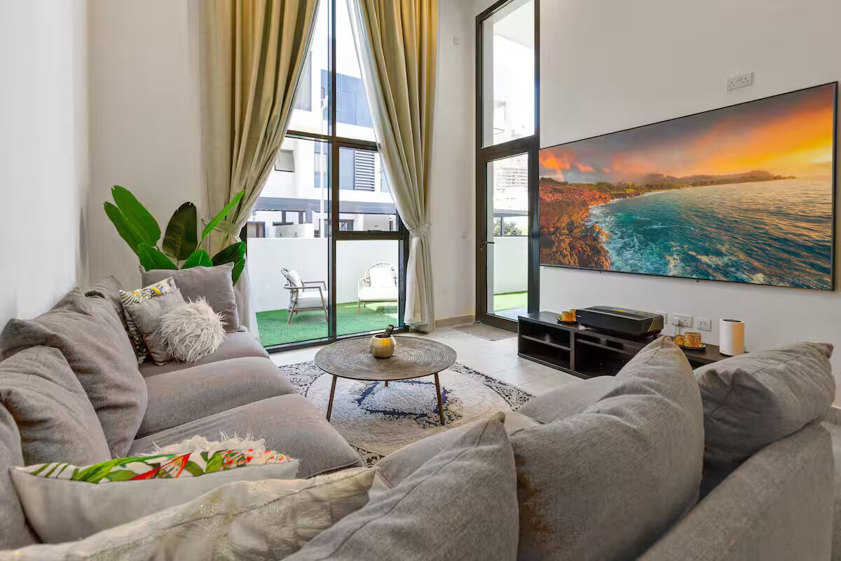 A modern living room with a large window, a sofa, a coffee table, and a painting of a coastal scene.