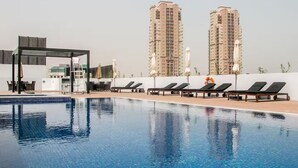 A swimming pool with lounge chairs and umbrellas, surrounded by tall residential buildings. - Spacious 2 BR + huge private garden in JVC (Jumeirah Village)