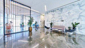 A modern lobby with a marble wall, a seating area with a sofa and chairs, and a large potted plant. - Spacious 2 BR + huge private garden in JVC (Jumeirah Village)