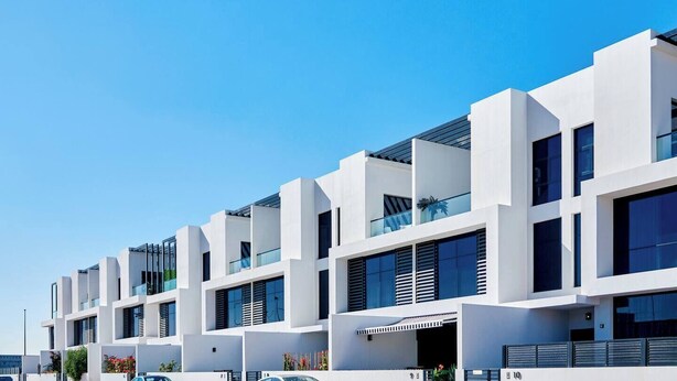 A modern multi-story building with white exterior walls, large windows, and balconies. - Spacious 2 BR + huge private garden in JVC (Jumeirah Village)