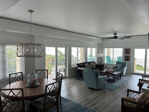 A spacious living room with a dining area, large windows, and a ceiling fan. - Coastal Charm- Oceanfront, 3rd floor, Land Transportation Included from Dock (Daufuskie Island)