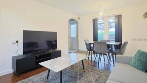 A modern living room with a flat-screen TV, a dining table with chairs, a sofa, and a large window. - Manchester 3-beds, Sleeps 6 With On-site Parking (Manchester)