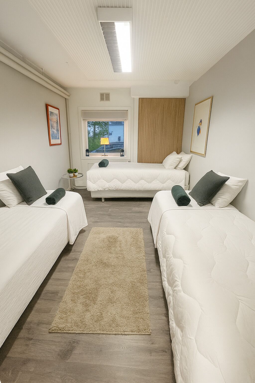 Habitación de hotel con dos camas individuales, un ventanal con vistas, una mesita con lámpara y una alfombra beige.