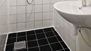 A bathroom with white tiled walls, a black tiled floor, a white sink, a mirror, and a shower with a handheld showerhead. - The Cozy Oslo Stay (Oslo)