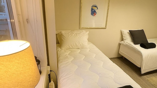 A hotel room with a bed, a bedside table with a lamp, a radiator, and a framed picture on the wall. - The Cozy Oslo Stay (Oslo)