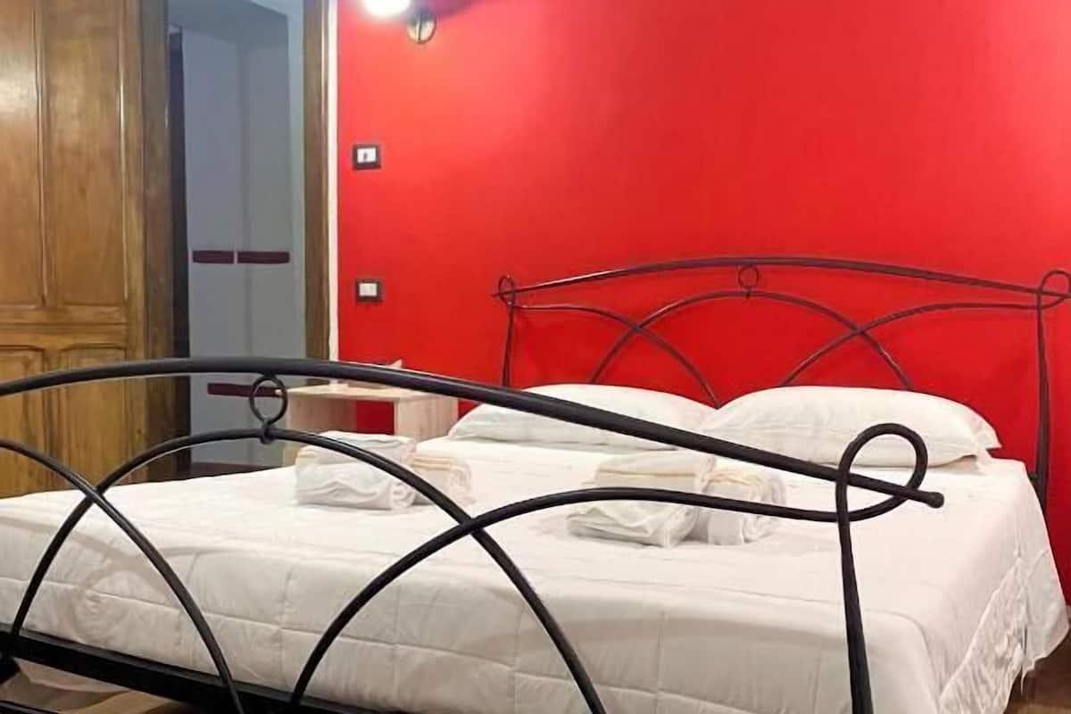 Ein Einzelbett mit Metallgestell, weißer Bettwäsche und einer roten Wand im Hintergrund.