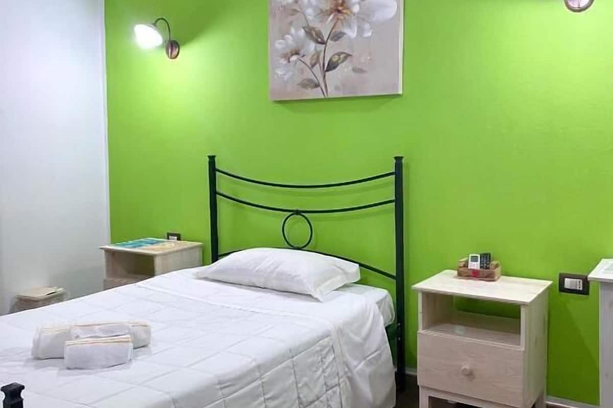 Ein Zimmer mit einem Bett, zwei Nachttischen, einer grünen Wand und einem Blumenbild.