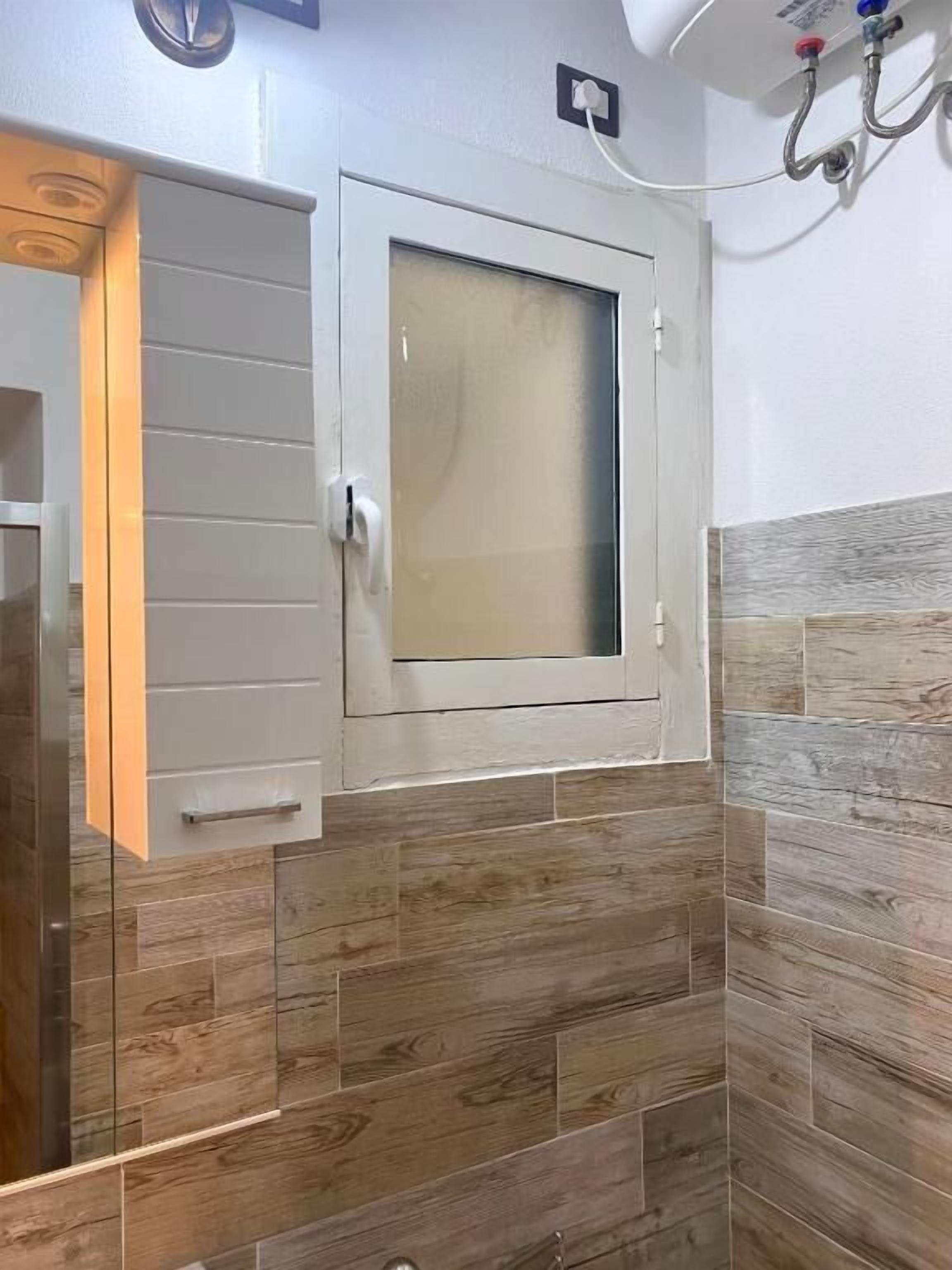 Casa de banho com painel de azulejos de madeira, janela de vidro jateado e porta branca com puxador.