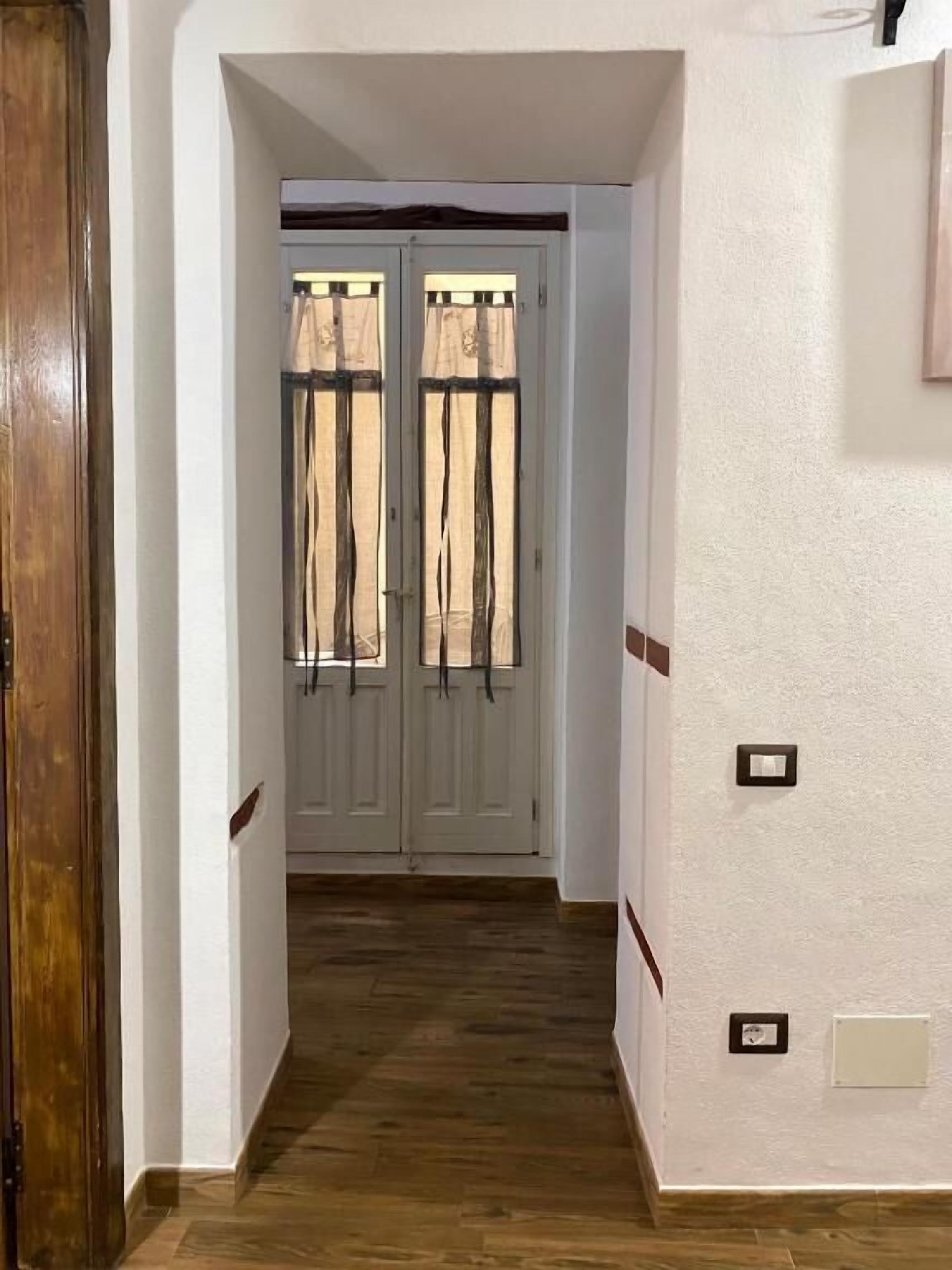 A hallway with a wooden floor leading to a white door with two glass panels.