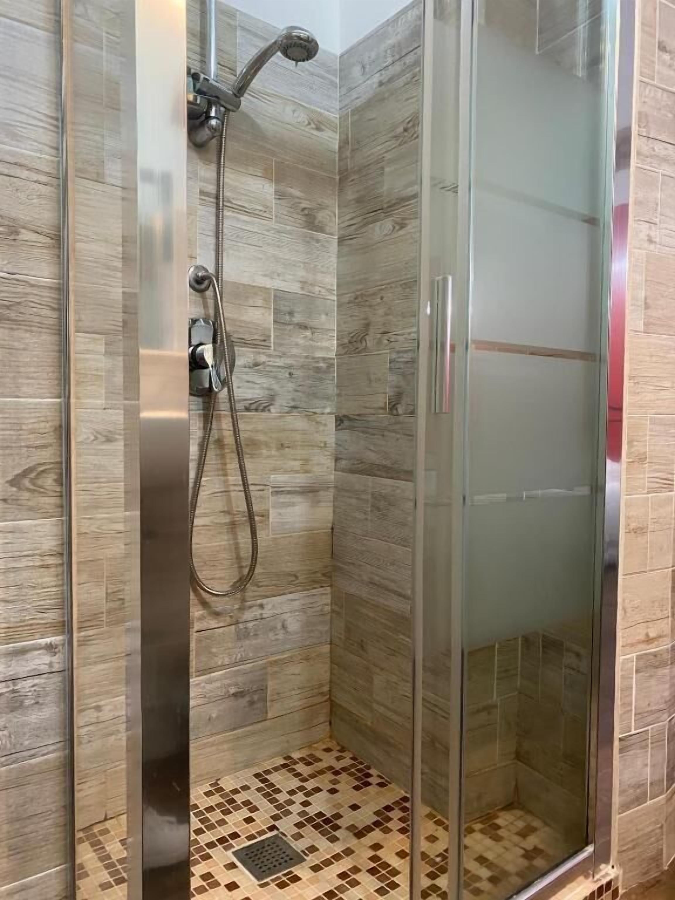 A glass-enclosed shower with a handheld showerhead and a wall-mounted faucet.