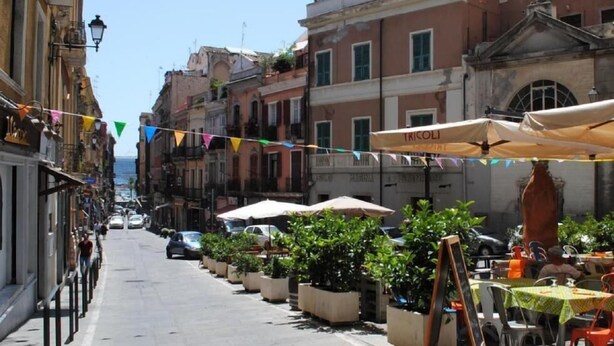A narrow street lined with buildings, outdoor seating with umbrellas, and potted plants. - Dani's House - affittacamere (Cagliari)