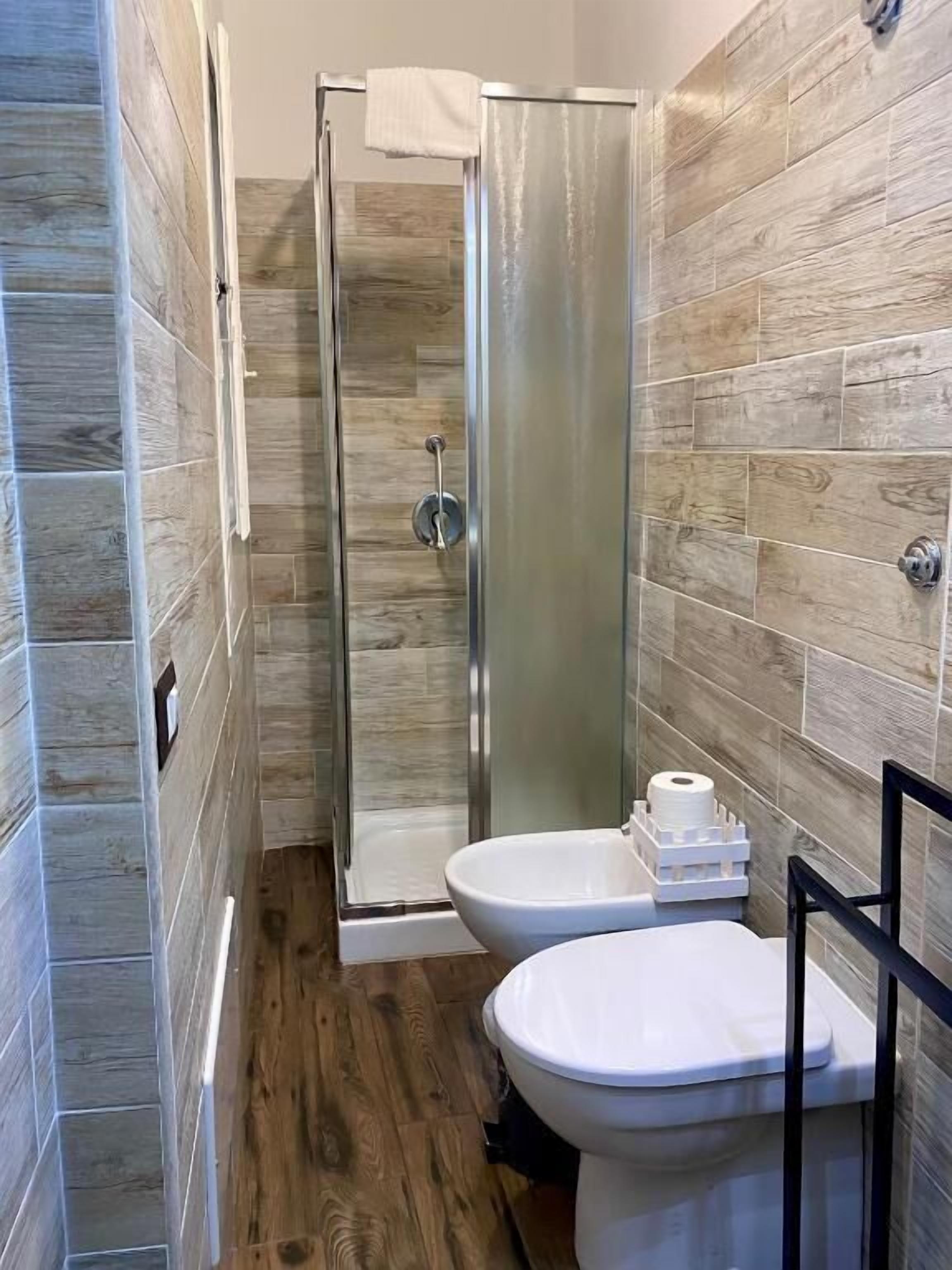A modern bathroom with a glass shower enclosure, two toilets, and a sink.